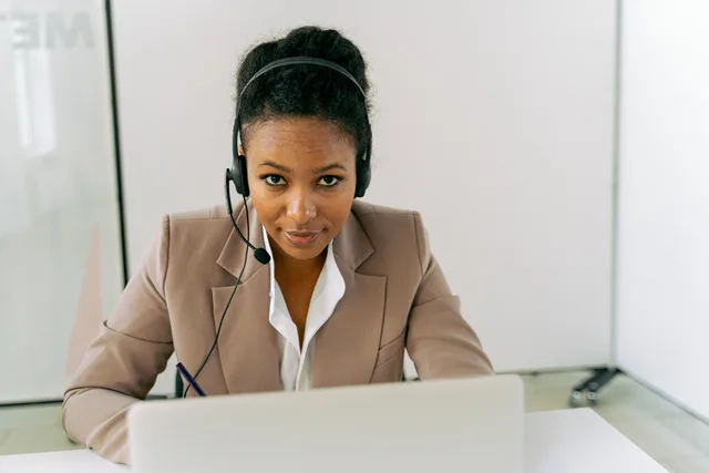 Confident woman in a call center setting, wearing a headset and suit, ready to assist. Checking CRM integration during a platform demo