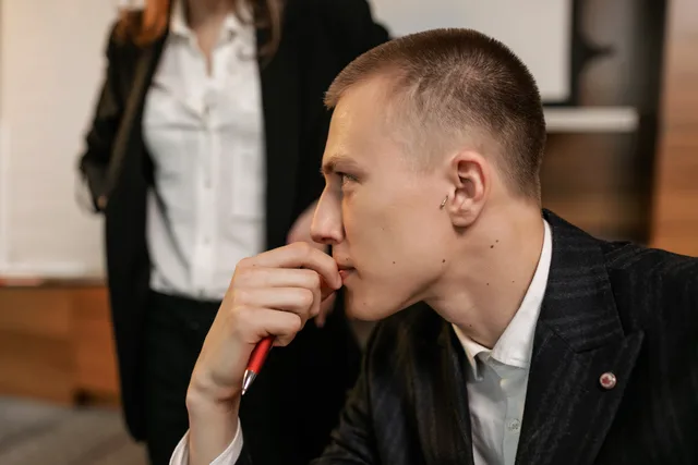 Side view of a thoughtful businessman holding a pen, contemplating in a modern office. Choosing practice exercises based on real tasks