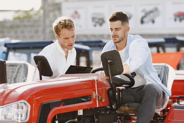 Two men discussing and evaluating the features of a red tractor outdoors in a dealership setting. Explaining who the new product is not suitable for