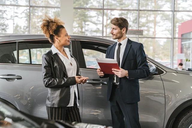 A woman discussing car purchase with a dealer inside a car dealership showroom. Identifying what prevents representatives from helping buyers