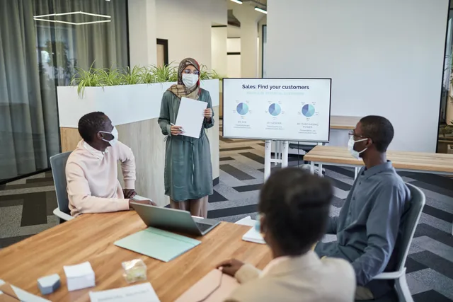 Colleagues wearing masks in a modern office discussing sales strategies. Keeping sales playbooks current after product changes