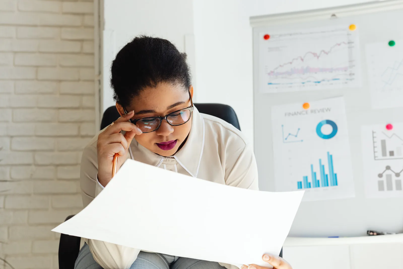 Focused businesswoman examining financial reports with graphs and charts on a whiteboard.
