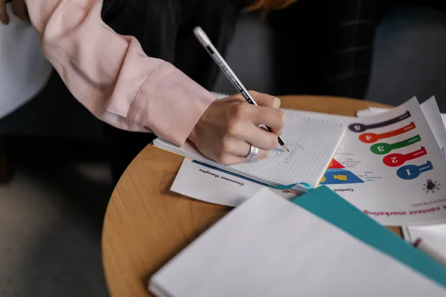 A person writing notes in a notebook with graphs on a table. Updating competitive notes after a product change