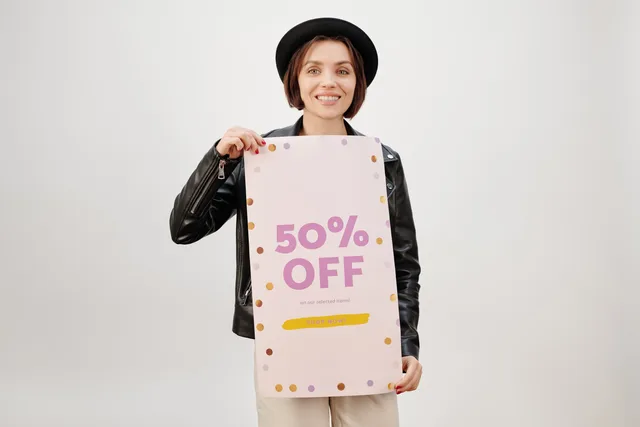Stylish woman smiling and holding a 50% off sale poster on a white background. Updating sales materials before external promotion